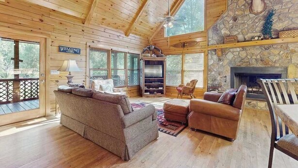 A wooden cabin interior with a fireplace, a sofa, a television, and a stone wall. - River Escape On The Toccoa River (Mineral Bluff)