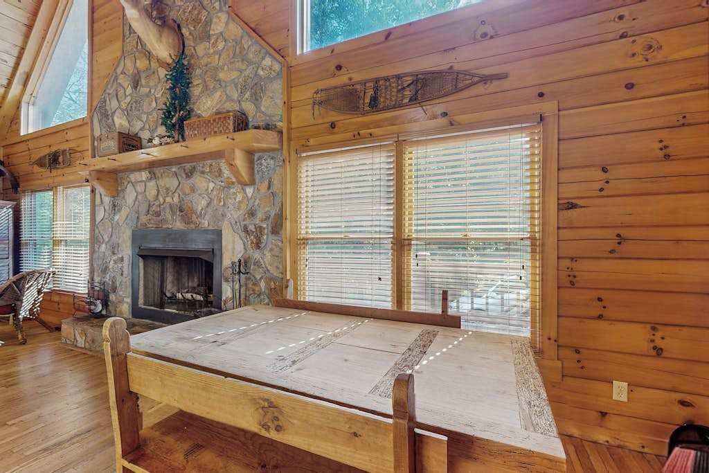 L’intérieur d’un chalet en bois est agrémenté d’une cheminée en pierre, de poutres apparentes et d’une grande fenêtre dotée de stores.