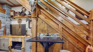 Eine Holztreppe führt zu einer Erkerzone mit Esstisch und Stühlen, einem Kamin und einem Fernseher.
