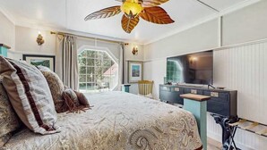 Ein Schlafzimmer mit einem großen Bett, einem Deckenventilator, einem Fernseher und einem Fenster.