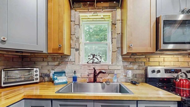 Eine Küche mit Steinrückwand, integriertem Fenster, Spülbecken aus Edelstahl, Toaster, Wasserkocher und Mikrowelle.