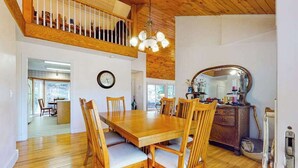Uma sala de jantar com uma mesa e cadeiras de madeira, um relógio na parede e um espelho à direita.