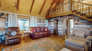 A log cabin interior with a wooden staircase, leather furniture, and a patterned rug. - Treehouse Retreat Stay (Sky Valley)