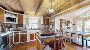 A spacious kitchen with wooden cabinets, a central island, and a dining area with a large table and chairs. - Treehouse Retreat Stay (Sky Valley)