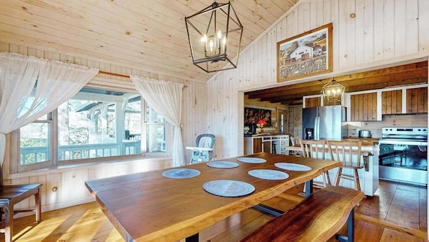 A wooden dining table with placemats, a kitchen area with a stove, and a hanging light fixture. - Treehouse Retreat Stay (Sky Valley)