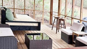 A room with a bed, two wicker sofas, a small stool, and a wooden table. - Bear's Den Sautee Cabin (Sautee Nacoochee)