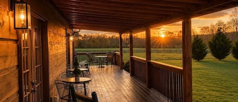 A wooden deck with outdoor seating and a view of a grassy field at sunset.