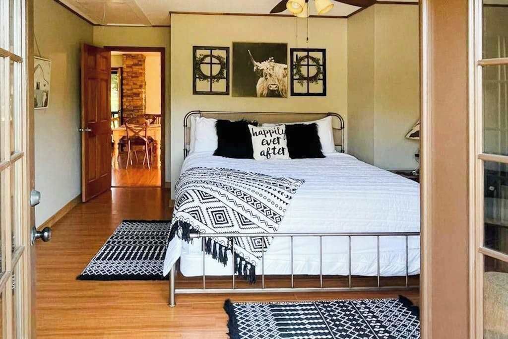 A bedroom with a bed, a door leading to a dining area, and a wall with framed pictures.