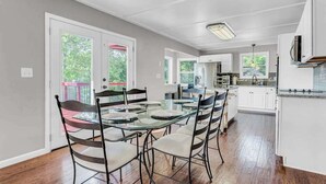 Una cocina amplia con gabinetes blancos, un comedor con mesa de vidrio y vistas al exterior.