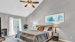 Un dormitorio con una cama, ventilador de techo, ventana con vistas y una puerta.