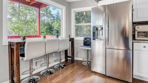 Una cocina con un refrigerador de acero inoxidable, un horno empotrado y una ventana con vistas a árboles.