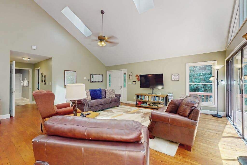 A spacious living room with a ceiling fan, a flat-screen TV, and a large window.