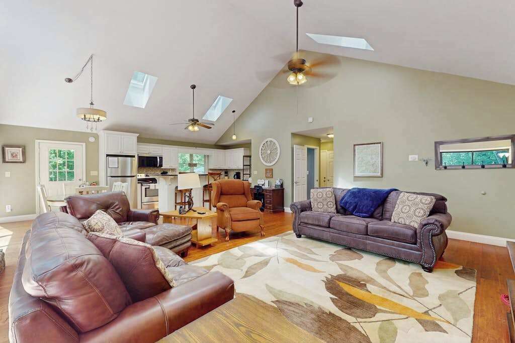 A spacious living area with a large brown leather sofa, a smaller sofa, a coffee table, and a ceiling fan.