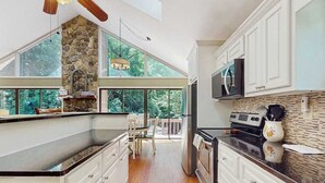 A kitchen with a stone wall, white cabinets, a large island, and a view of the outdoors. - Creekside Retreat Stay (Morganton)