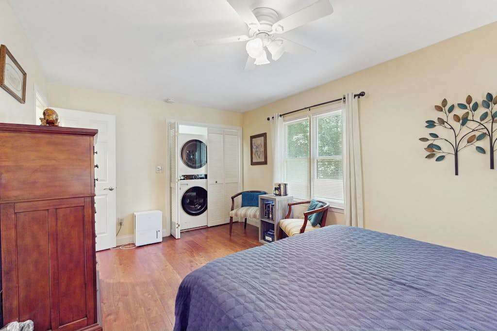 A bedroom with a bed, a ceiling fan, a washing machine, a chair, and a window with curtains.
