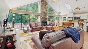 A spacious living room with leather sofas, a fireplace, and large windows offering a view of the outdoors. - Creekside Retreat Stay (Morganton)