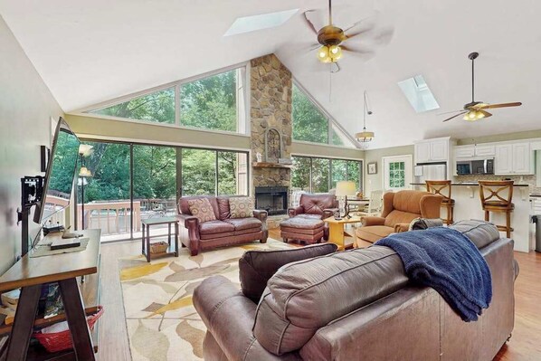 Ein großzügiges Wohnzimmer mit Ledersofas, einem Kamin und großen Fenstern mit Blick ins Freie.