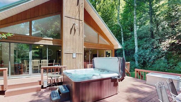A modern wooden cabin with a hot tub, outdoor seating, and large windows overlooking a forest. - Creekside Retreat Stay (Morganton)
