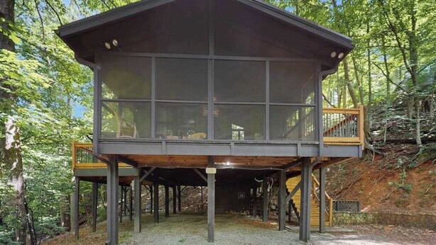 Eine moderne, mehrstöckige Holzhütte mit großen Fenstern, umgeben von einem Wald.