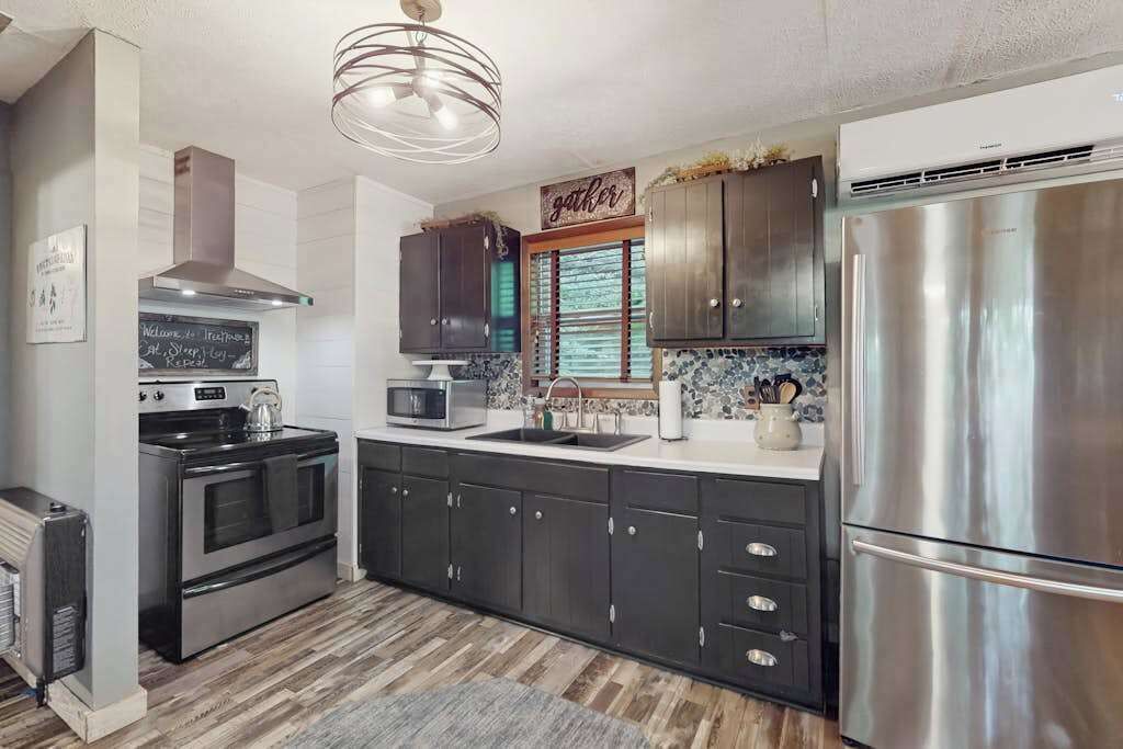 A modern kitchen with stainless steel appliances, dark cabinetry, and a chalkboard sign.