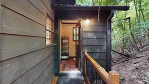 Eine Holzhütte mit Veranda, einem Eingang und einem bewaldeten Hintergrund.