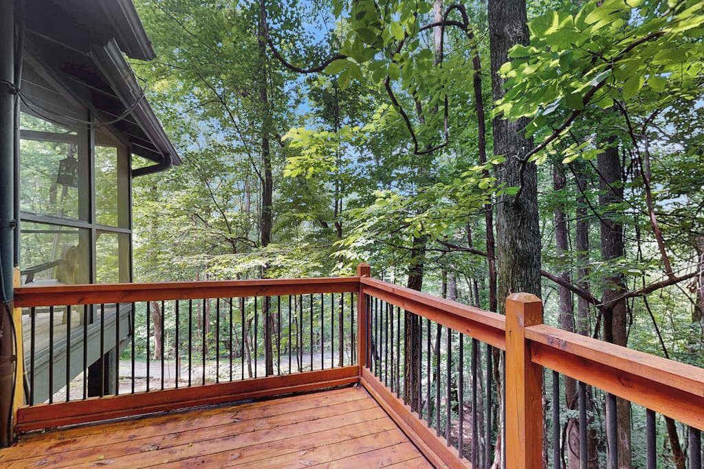 A wooden deck with a railing, surrounded by trees.