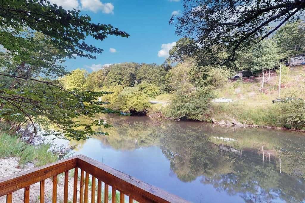 A serene lakeside view with a wooden deck, surrounded by lush greenery and trees.