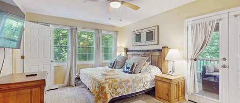 A bedroom with a bed, a ceiling fan, a nightstand, a TV, and a door leading to a balcony.