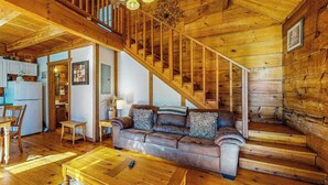 A wooden interior with a staircase, a sofa, a coffee table, and a kitchen area.