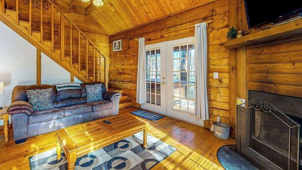 A log cabin interior with a sofa, coffee table, fireplace, and a TV mounted on the wall.