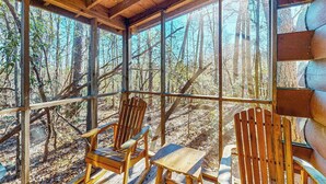 A cabin with large windows, wooden chairs, and a table.