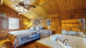 A wooden cabin room with a bed, a dresser, a large bathtub, and a ceiling fan.