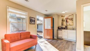 A living room with a sofa, a kitchen with cabinets and a microwave, and a door leading outside.