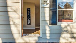 A house entrance with a 'WELCOME' sign, a doormat, and a window with blinds.