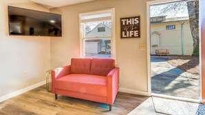 A living room with a sofa, a flat-screen TV, a window, and a door leading outside.