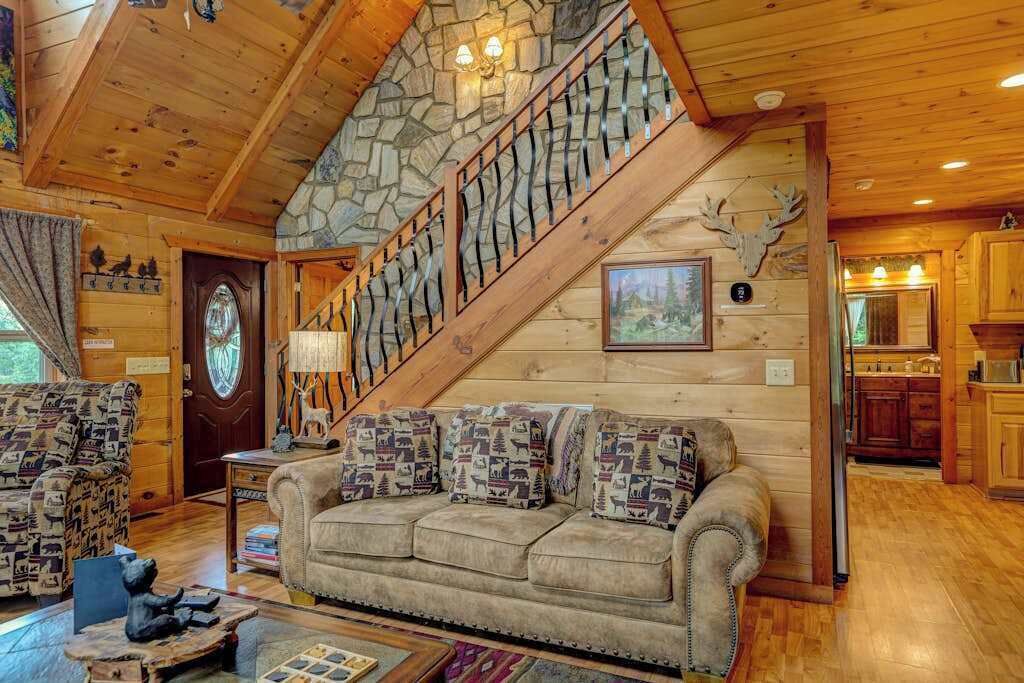 L’intérieur chaleureux d’un chalet avec un escalier en pierre, un plafond en bois, un canapé agrémenté de coussins à motifs et une statue d’ours.