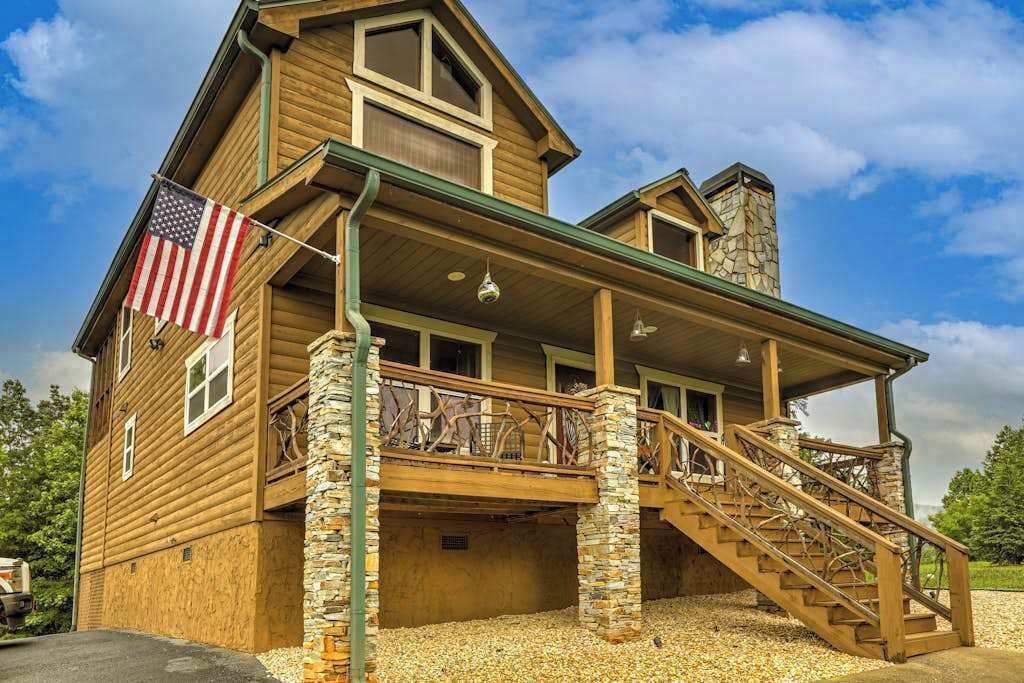 A wooden house with a stone chimney, a balcony with railings, and an American flag.