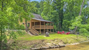 A log cabin with a porch, surrounded by trees and a stream. - River Fishing Cabin - Dog Friendly (Lakemont)