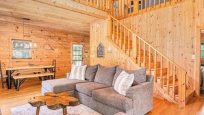 A wooden cabin interior with a staircase, a sectional sofa, a dining table, and a wooden coffee table. - River Fishing Cabin - Dog Friendly (Lakemont)