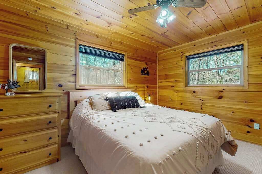 Ein Schlafzimmer einer Holzhütte mit einem Bett, einem Schminktisch und zwei Fenstern.