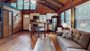 A cozy cabin interior with a kitchen, dining area, and a living room with a sofa and a lamp.