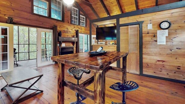 A rustic wooden interior with a large wooden table, a ceiling fan, and a television.