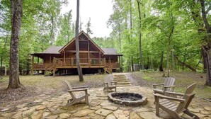 A cabin with a stone patio, Adirondack chairs, and a fire pit. - Toccoa River Run Cabin (Mineral Bluff)