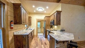 A kitchen with wooden cabinets, granite countertops, a stone island, and a microwave. - Toccoa River Run Cabin (Mineral Bluff)
