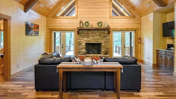 A log cabin interior with a stone fireplace, a sofa, a table, and a television. - Toccoa River Run Cabin (Mineral Bluff)