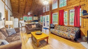 Interior espacioso de una cabaña con techo de madera, un sofá, un sillón, una mesa de comedor y una zona de cocina.