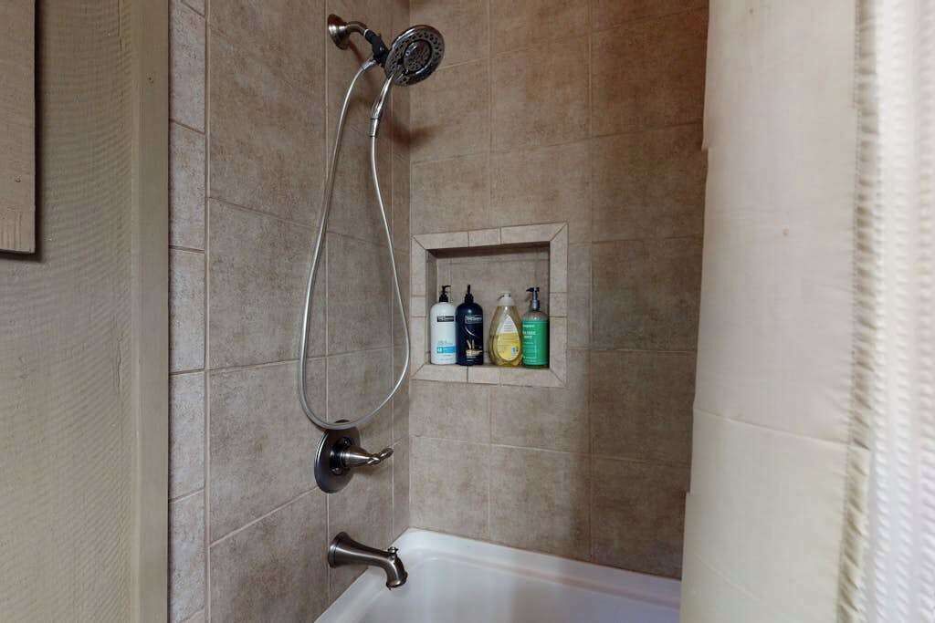 Een badkamer met een douche, een bad en een plank met toiletartikelen.