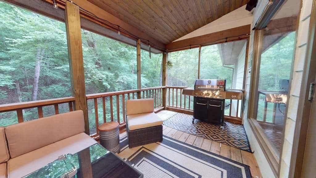A covered outdoor deck with a grill, seating, and a view of the forest.