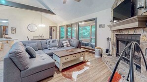 Ein modernes Wohnzimmer mit einem Ecksofa, einem Kamin, einem Deckenventilator und großen Fenstern.