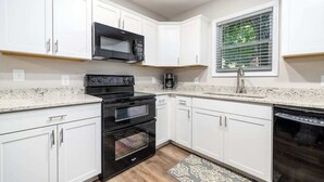 Una cocina moderna con armarios blancos, un microondas negro, una estufa y un lavavajillas.